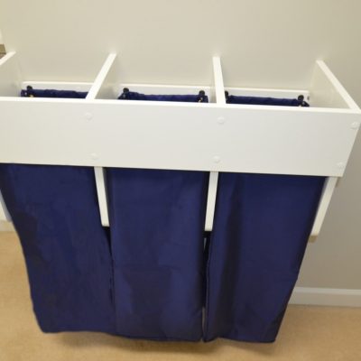 Close up peek at our (not yet!) dirty laundry sorter. Three drawstring bags lift off of internal hooks for convenience.